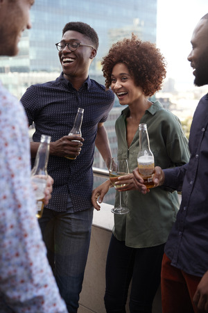 Smiling creative business colleagues socialising with drinks after work, verticalの写真素材