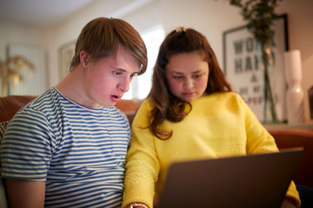 Young Downs Syndrome Couple Sitting On Sofa Using Laptop At Homeの写真素材