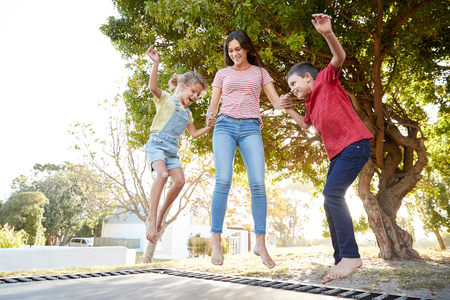 Siblings With Teenage Sister Playing On Outdoor Trampoline In Gardenの写真素材