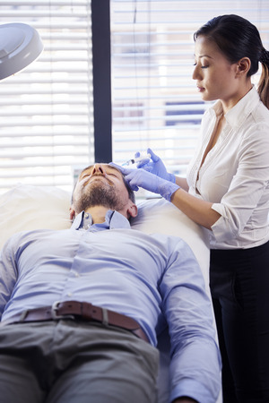 Female Beautician Giving Mature Male Patient Botox Injection In Foreheadの写真素材