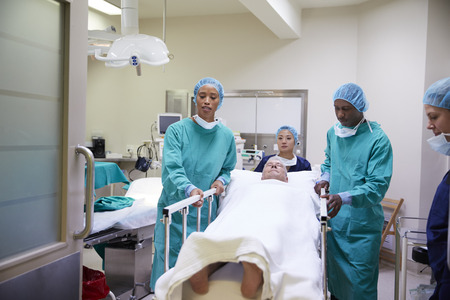 Surgical Team Wheeling Senior Male Patient Out Of Hospital Operating Theatre