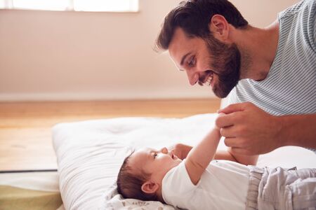 Loving Father Lying With Newborn Baby On Bed At Home In Loft Apartmentの写真素材