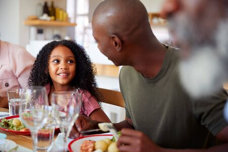 Multi-Generation Family Sitting Around Table At Home Enjoying Meal Together