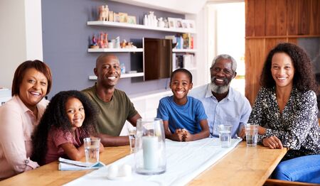 Portrait Of Multi-Generation Family Sitting Around Table At Home Enjoying Meal Together
