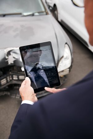 Insurance Loss Adjuster Taking Picture With Digital Tablet Of Damage To Car From Motor Accidentの写真素材