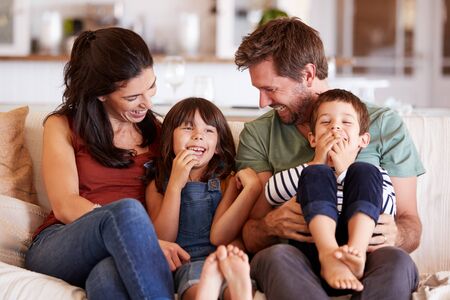 Mid adult white couple and their two young children sitting on a sofa at home smiling at each otherの写真素材
