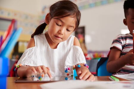 Female Pupil In Elementary School Drawing Using Digital Tablet In Classroom