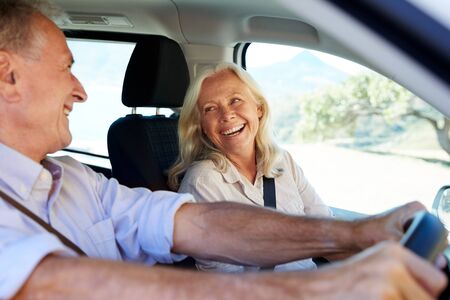 Senior white couple driving in their car, looking at each other, side view, close upの写真素材