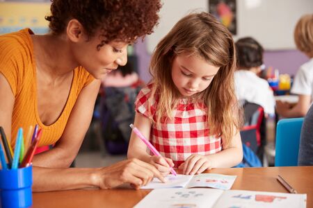 Elementary School Teacher Giving Female Pupil One To One Support In Classroom