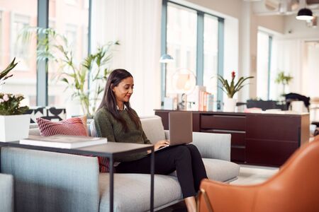 Businesswoman Sitting On Sofa Working On Laptop At Desk In Shared Workspace Officeの写真素材