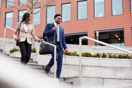 Businessman And Businesswoman Commuting To Work Walking Down Steps Outside Office Building