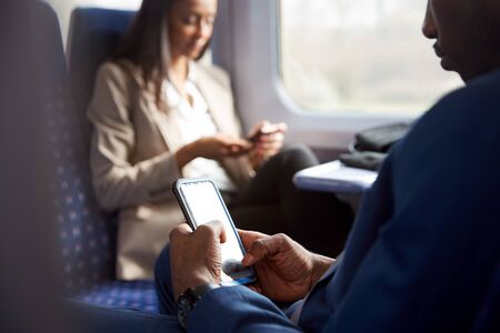 Close Up Of Business Passengers Sitting In Train Commuting To Work Looking At Mobile Phonesの写真素材