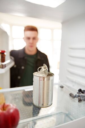 Young Man Looking Inside Refrigerator Empty Except For Open Tin Can On Shelfの写真素材