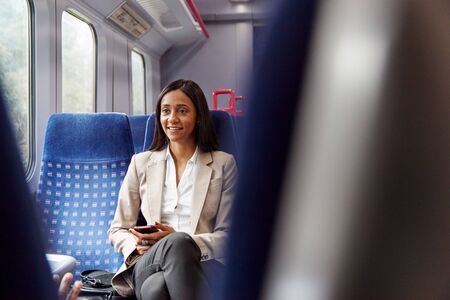 Businesswoman Sitting In Train Commuting To Work Checking Messages On Mobile Phoneの写真素材