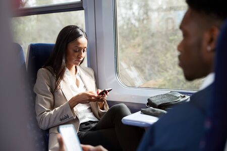 Business Passengers Sitting In Train Commuting To Work Looking At Mobile Phonesの写真素材