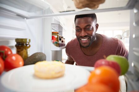 View Looking Out From Inside Of Refrigerator As Man Opens Door And Reaches For Unhealthy Donutの写真素材