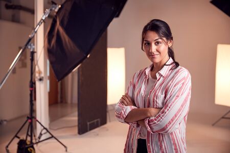 Portrait Of Smiling Female Photographer Standing In Studio With Lighting Equipmentの写真素材