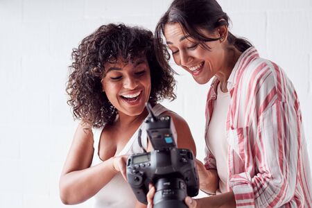 Smiling Female Photographer Holding Camera With Model In Studio Portrait Sessionの写真素材