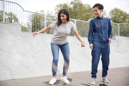 Two Female Friends Riding On Skateboards In Urban Skate Parkの写真素材
