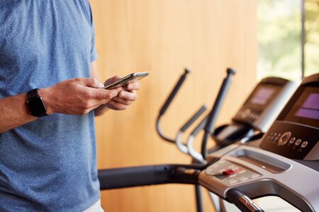 Close Up Of Man Exercising On Treadmill At Home Wearing Smart Watch Checking Mobile Phoneの写真素材