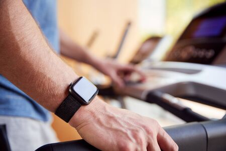 Close Up Of Man Exercising On Treadmill Wearing Smart Watch Checking Mobile Phone