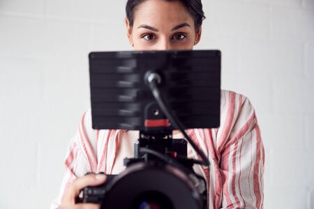 Female Videographer With Video Camera Filming Movie In White Studio