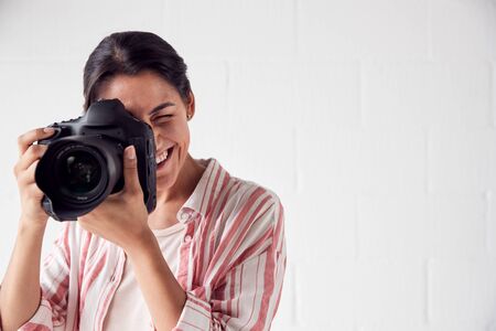 Female Photographer With Camera On Photo Shoot Against White Studio Backdropの写真素材
