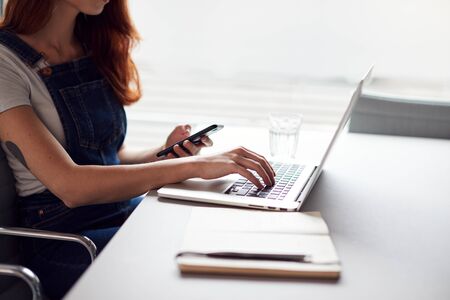 Casually Dressed Young Businesswoman Working On Laptop In Modern Workplace Checking Text Messages