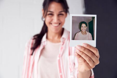 Portrait Of Female Photographer On Photo Shoot Holding Up Instant Polaroid Print In Studioの写真素材