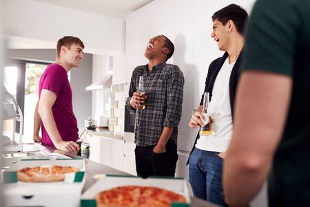 Group Of Male College Students In Shared House Kitchen Drinking Beer And Eating Pizza Togetherの写真素材
