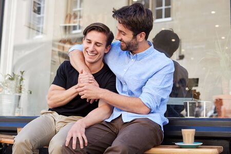 Loving Male Gay Couple Sitting Outside Coffee Shop Hugging