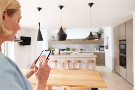 Close Up Of Woman Using App On Smart Phone To Control Central Heating Temperature In Houseの写真素材