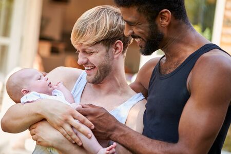 Loving Male Same Sex Couple Cuddling Baby Daughter At Home In Garden Togetherの写真素材