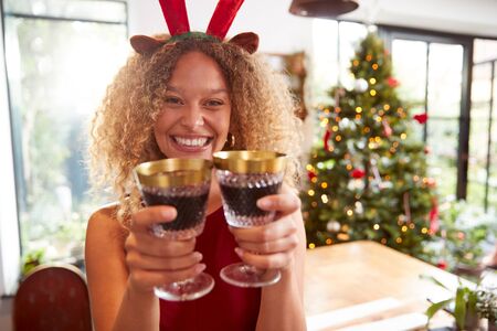 Woman Wearing Fancy Dress Antlers Holding Two Glasses Of Wine For Toast On Christmas Dayの写真素材