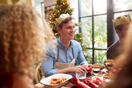 Group Of Friends Sitting Around Table At Home For Christmas Dinner Reading Jokes From Crackersの写真素材