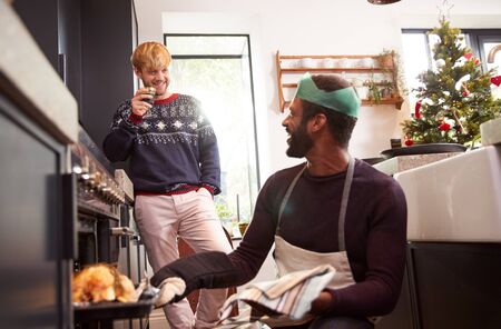 Gay Male Couple At Home In Kitchen Cooking Dinner On Christmas Day Together