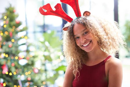 Portrait Of Woman Wearing Fancy Dress Antlers Standing Next To Christmas Tree At Homeの写真素材