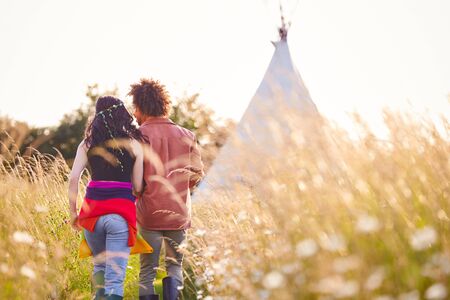 Young Romantic Couple Walking Through Field Towards Teepee On Summer Camping Vacation