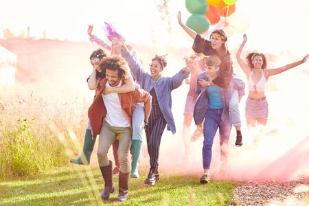 Group Of Friends Walking Back To Tent After Outdoor Music Festival With Balloons And Smoke Flareの写真素材