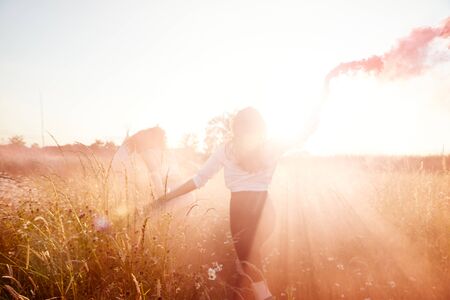 Rear View Of Two Female Friends Camping At Music Festival Running Through Field With Smoke Flareの写真素材