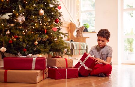 Excited Boy Opening Presents By Tree On Christmas Morningの写真素材