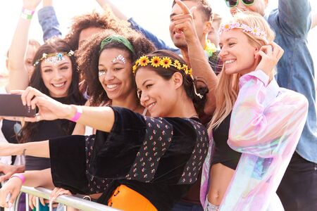 Young Friends In Audience Behind Barrier At Outdoor Music Festival Posing For Selfieの写真素材