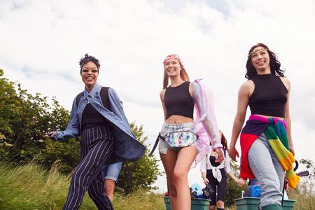 Group Of Excited Young Female Friends Carrying Camping Equipment Through Field To Music Festivalの写真素材