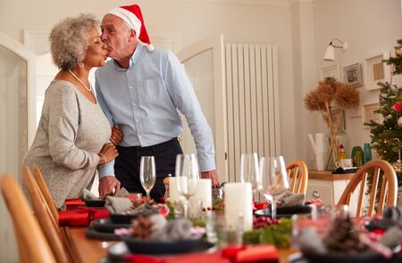 Loving Senior Couple At Home Setting And Decorating Table For Meal On Christmas Dayの写真素材