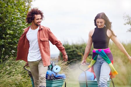 Young Couple Pulling Trolley Filled With Camping Equipment Through Field To Music Festivalの写真素材