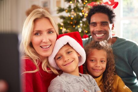 Portrait Of Family Posing For Selfie Sitting On Sofa Celebrating Christmas Together