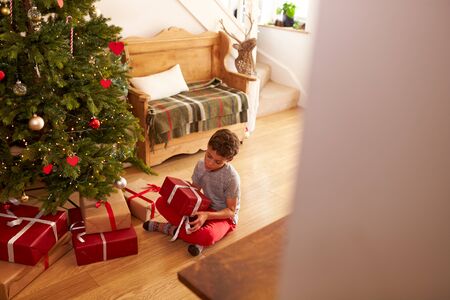 Excited Boy Opening Presents By Tree On Christmas Morningの写真素材