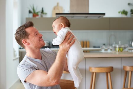 Loving Father Holding 3 Month Old Baby Daughter In Kitchen At Home