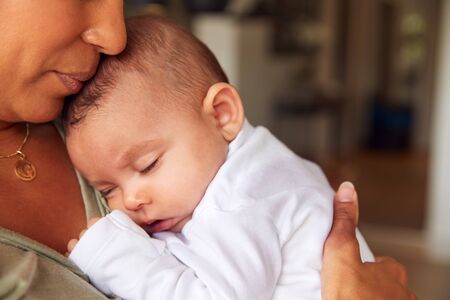 Close Up Of Loving Mother Holding Sleeping 3 Month Old Baby Daughter In Kitchen At Homeの写真素材