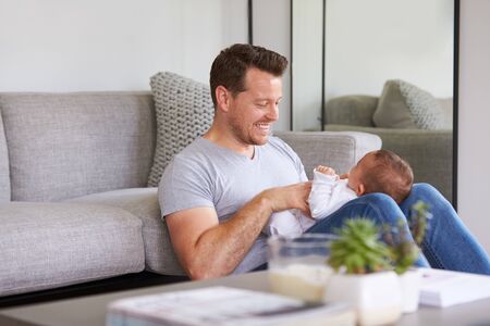 Baby Daughter Lying On Fathers Lap As He Plays Game With Her At Home